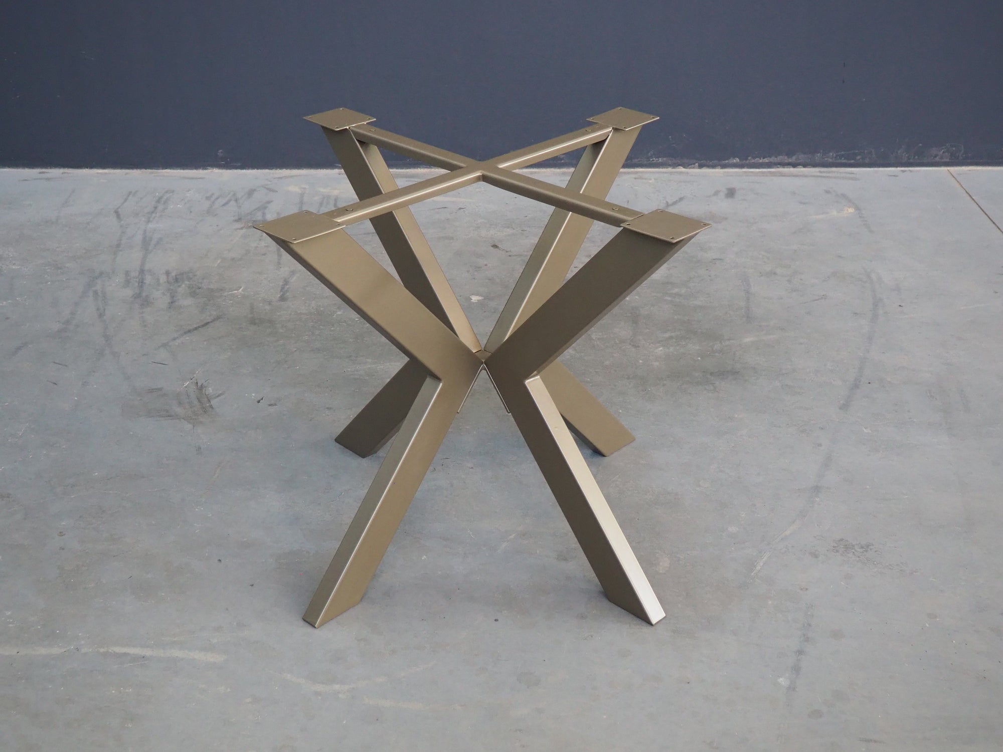A BRONZE metal table base designed for supporting a round table top, displayed on a wooden floor against a white background.
