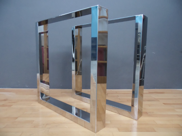 A set of two stainless steel wide tube dining table legs reflecting light on a dark background.
